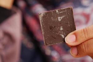 Hand holding a piece of dark chocolate in a vibrant setting photo
