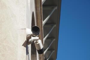 Security camera mounted on a building against a clear blue sky photo