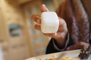 Hand holding a white cube shaped condiment container at a meal photo