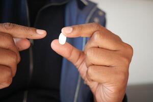 Person holds a white pill between fingers in a casual setting photo