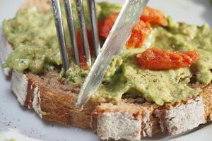 Slicing through toasted bread topped with avocado and tomatoes photo