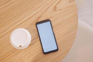 Smartphone on wooden table next to coffee cup in cozy cafe setting photo