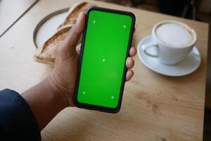 Holding smartphone with blank screen while seated at cafe table photo