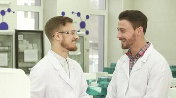 Two laboratory technicians share a light-hearted conversation in a modern lab video