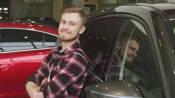 Confident man giving a thumbs up while leaning on a sleek new car at the dealership video