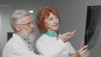 In a modern hospital setting, an elderly female doctor engages in a focused discussion with her male colleague as they examine an MRI scan. Their expressions reflect deep concentration and collaboration, showcasing the essence of teamwork in healthcare video