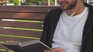 The handsome man joyfully turns the pages of a book while sitting on a park bench video