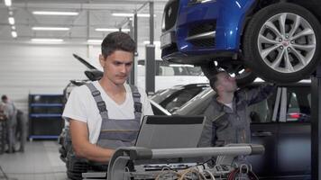 enfocado joven coche mecánico utilizando ordenador portátil para diagnósticos en un ocupado garaje video