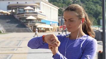 A young, attractive woman stands on a vibrant riverwalk, intently checking her watch while wearing stylish headphones. With a determined expression, she suddenly sprints out of the frame, embodying energy and urgency video