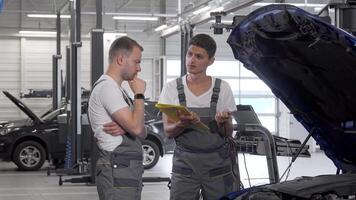 Two car mechanics engaged in a focused discussion over an open hood video