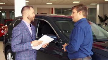 In a sleek car dealership, a well-dressed seller presents the contract details to a satisfied buyer, both smiling as they shake hands. The atmosphere is filled with excitement and professionalism, showcasing a successful deal on a new vehicle video