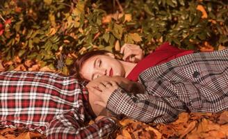 young couple in love lying on the ground in autumn park on yellow foliage. they hug each other, the sun brightly illuminates them. concept of romance, falling in love, relaxation photo
