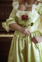 close-up of a medieval dress corset and corset. pearls on the neck. soft green rococo style dress. red rose in hands. photo without a face. black piano in the background.