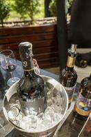 Odessa, Ukraine - April 05, 2025. A bottle of champange in an ice bucket at a hotel outdoors on a spring day. In the background, a bottle of wine and glasses. The blurred background includes a wine glass. photo