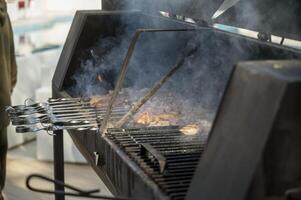 cooking meat on grill at barbecue party in summer garden. Food, people and family time concept. pork on skewers roasting on coals in large metal grill device. smoke from fire, no people photo