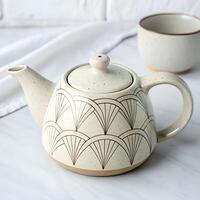 A ceramic teapot with a geometric pattern, accompanied by a matching teacup, set against a white marble surface and a white brick wall photo