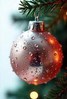 A pink christmas ball with water drops hanging from a christmas tree, with a blurry background photo