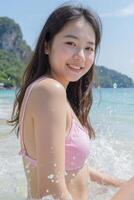 An asian girl, light skin, long brown hair, pink bikini, smiling in front of the sea with a mountain in the background photo