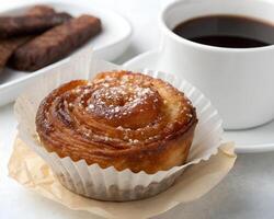 A caramelized kouign-amann pastry in a paper wrapper with crisp edges, sugar glistening, and a side of black coffee photo