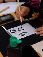 Person practicing calligraphy with brush and ink, close-up of a person's hand delicately applying ink with a brush to a sheet of paper, practicing Chinese calligraphy photo