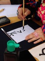 Person practicing Calligraphy with brush and ink. Close-up of a person's hand delicately applying ink with a brush to a sheet of paper, practicing Chinese calligraphy. photo