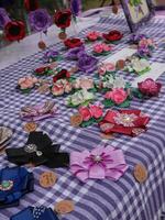 Handmade Floral Brooches and Bows at a Market Stall. A vibrant display of handmade flower brooches and bows, arranged on a checkered tablecloth at a market stall. photo