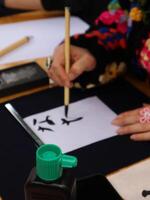 Person practicing calligraphy with brush and ink.Close-up of a person's hand delicately applying ink with a brush to a sheet of paper, practicing Chinese calligraphy. photo