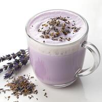 A glass mug filled with a frothy lavender honey latte topped with foam and seeds, in a white background photo