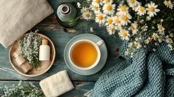 Cozy arrangement featuring cup of herbal tea, chamomile flowers, essential oils, and soft textiles on rustic wooden table photo