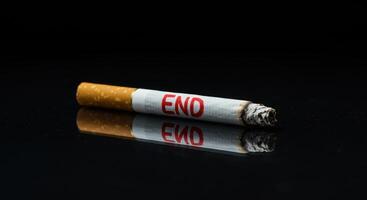 Close up of a lit cigarette with the word END in red on its side, symbolizing quitting smoking and the health risks associated with tobacco use on a reflective surface. photo