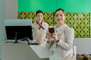 Smiling woman holding passport and boarding pass at airport check-in counter with airline staff in background, ready for international travel adventure photo