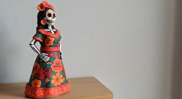 Hand-painted Catrina figure with floral patterns standing on wooden shelf, minimalist white wall background with copy space photo