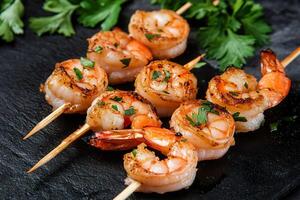 Grilled shrimp skewers with herbs on black slate. photo
