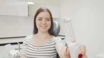 uma alegre jovem mulher orgulhosamente detém dela elétrico escova de dente, irradiando felicidade dentro uma brilhante dental clínica. isto vibrante cena enfatiza a importância do dental Cuidado, exibindo dela comprometimento para uma saudável sorrir video