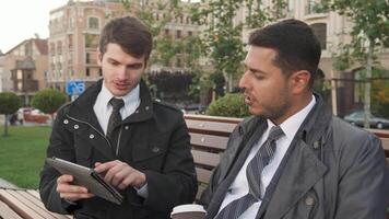 Two men engage in a focused discussion while reviewing a tablet video