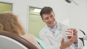 Cheerful girl beams at the camera while dentist showcases teeth model video