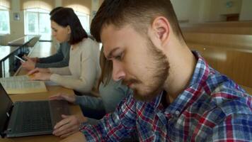 Focused female student engaged with laptop in a bustling lecture hall video