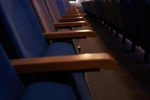 Some of the chairs are upholstered in fabric. A conference room with rows of empty blue chairs. With space to copy photo