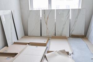 A large marble tile for walls measuring 120 by 60 is displayed in a row, the selection of a pattern on the tile for laying on the walls. On the background of a window under daylight photo