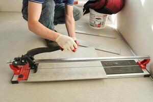 An installation for cutting large ceramic tiles into smaller tiles with precise dimensions. Close-up of the master cutting the tile into two parts with a machine. photo