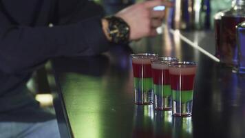 Vibrant shots of colorful cocktails on a sleek bar table with a man using his smartphone video