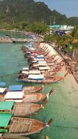 Aerial view of colorful traditional longtail boats anchored along white sand beach with turquoise water on Phi Phi Island, Thailand. video