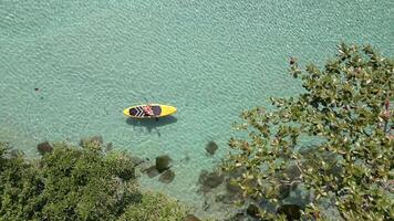 Top down view of woman paddleboarding on turquoise water near lush tropical island on sunny day, Thailand. Concept of freedom, adventure, and summer travel. video