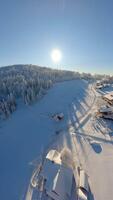 FPV drone flight above a snowy ski resort and wide ski slope in the mountains on a clear, sunny winter day video