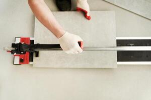 Close-up of the master cutting the tile into two parts with a machine. A machine for cutting large ceramic tiles into smaller tiles with precise dimensions. photo