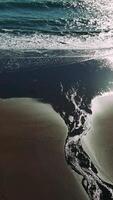 Sunlight gleaming on wet shoreline, stream merging with ocean waves, creating sparkling coastal landscape at golden hour video