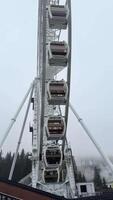 Foggy landscape revealing mist-shrouded forested hills with vintage ferris wheel gondolas rotating slowly against cloudy background, creating atmospheric scenic view video