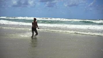 A hilarious middle-aged office escapee runs joyfully through ocean waves, his carefree sprint along a vast sandy beach under blue skies symbolizing the perfect break from routine. video