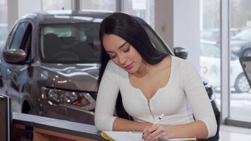 A confident woman beams with joy as she signs the paperwork for her new car, surrounded by a sleek vehicle in a modern dealership. This vibrant scene captures the excitement of ownership and the thrill of making a significant investment in her future video