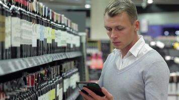 Thoughtful man selecting wine while checking details on a tablet video